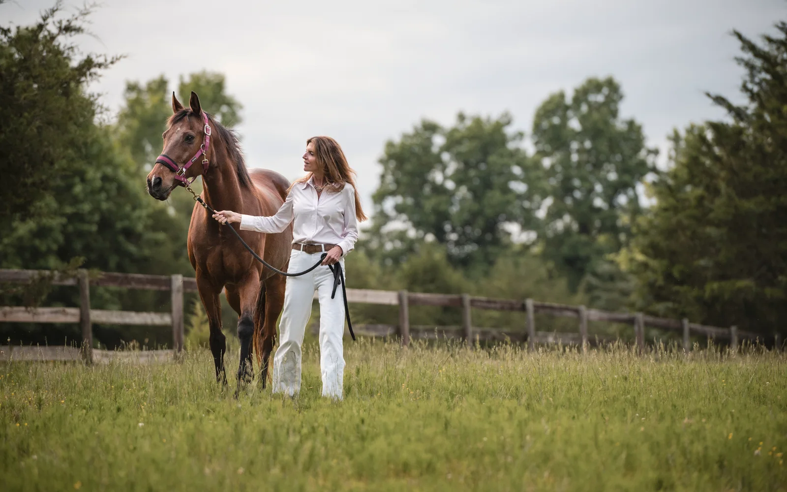Denise confidently walking with her horse through a fenced pasture