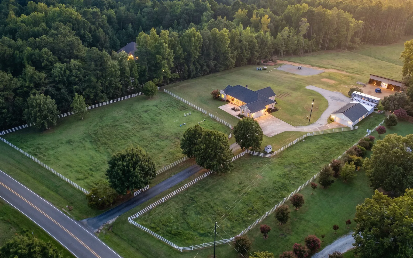 Aerial view of an equestrian property with fenced pastures, a residence, barn, arena, and surrounding woodland.