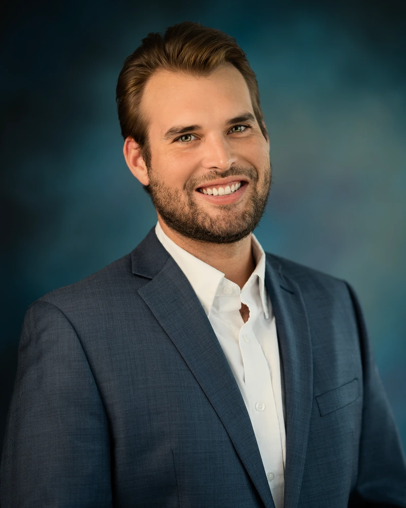 Man in a navy suit against a richly colored teal studio background