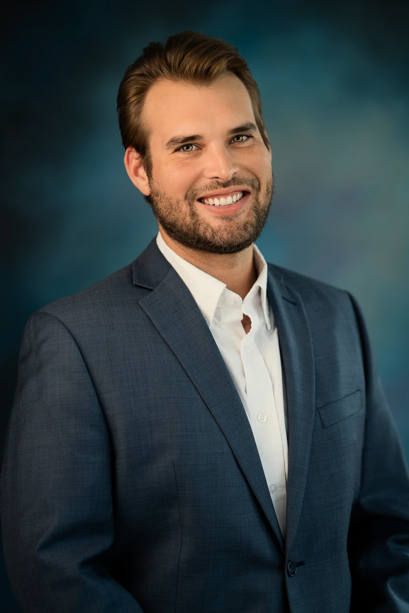 Man in a navy suit against a richly colored teal studio background