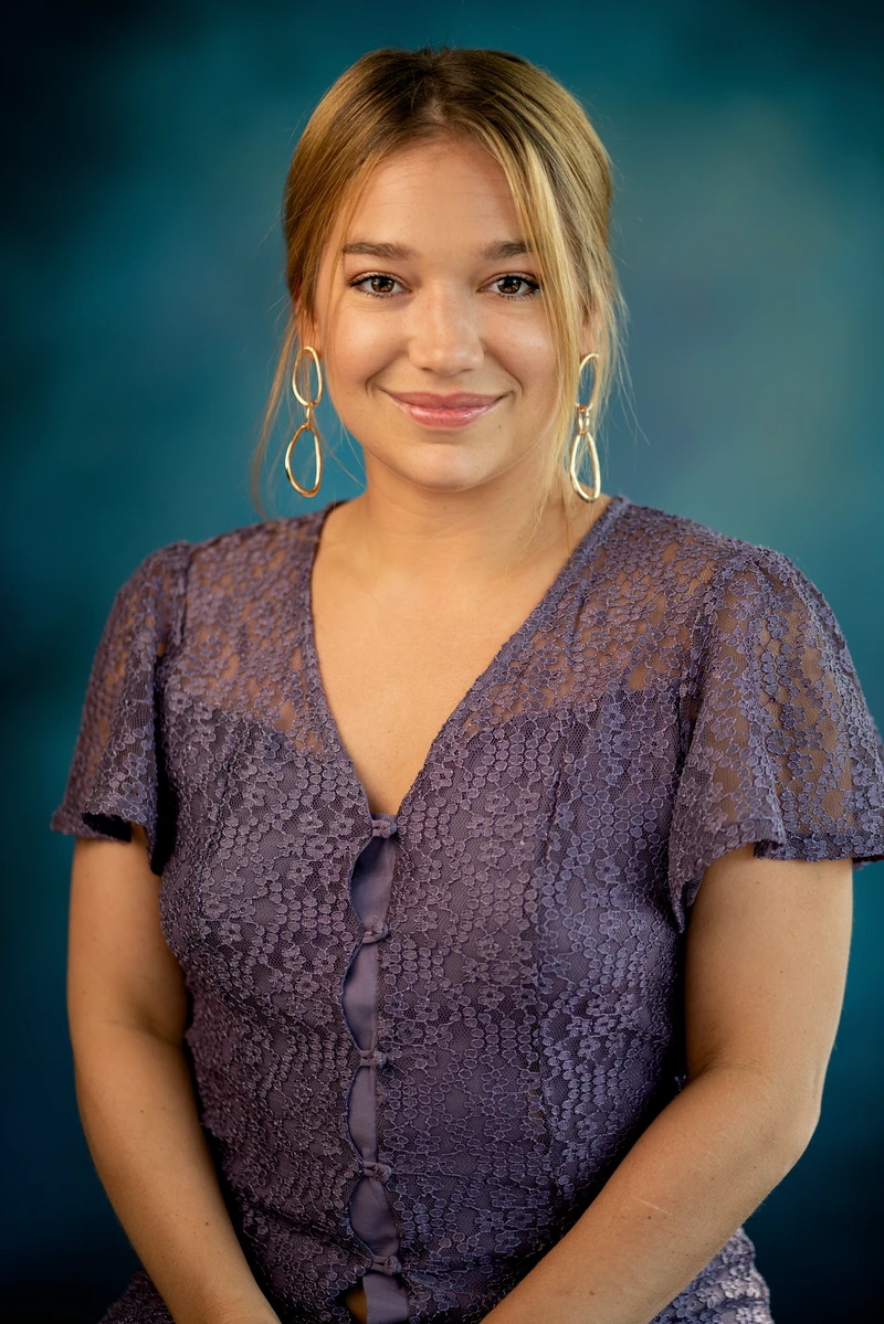 Woman in a purple blouse against a richly colored teal studio background