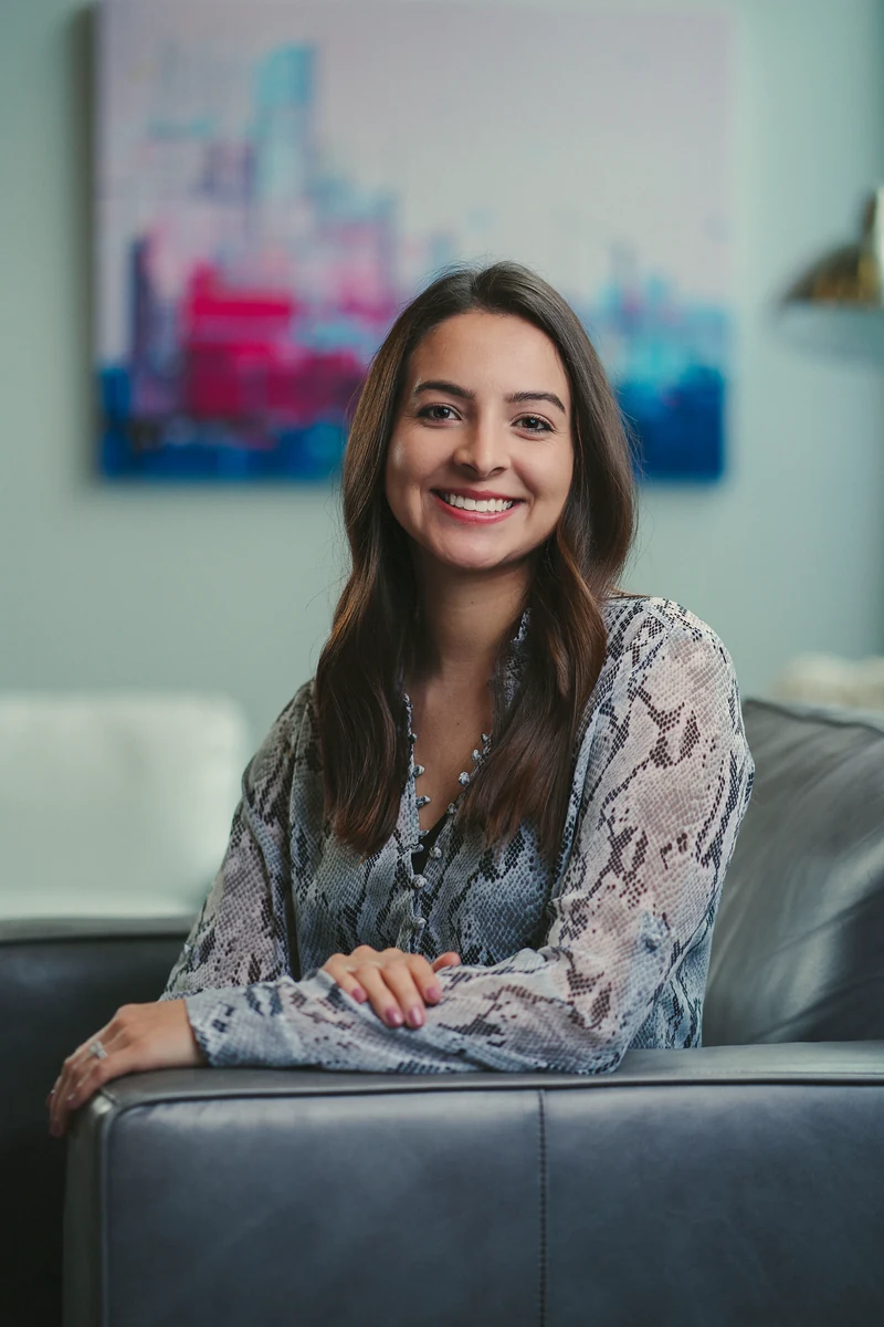 Woman in a patterned blouse seated in a cool gray office
