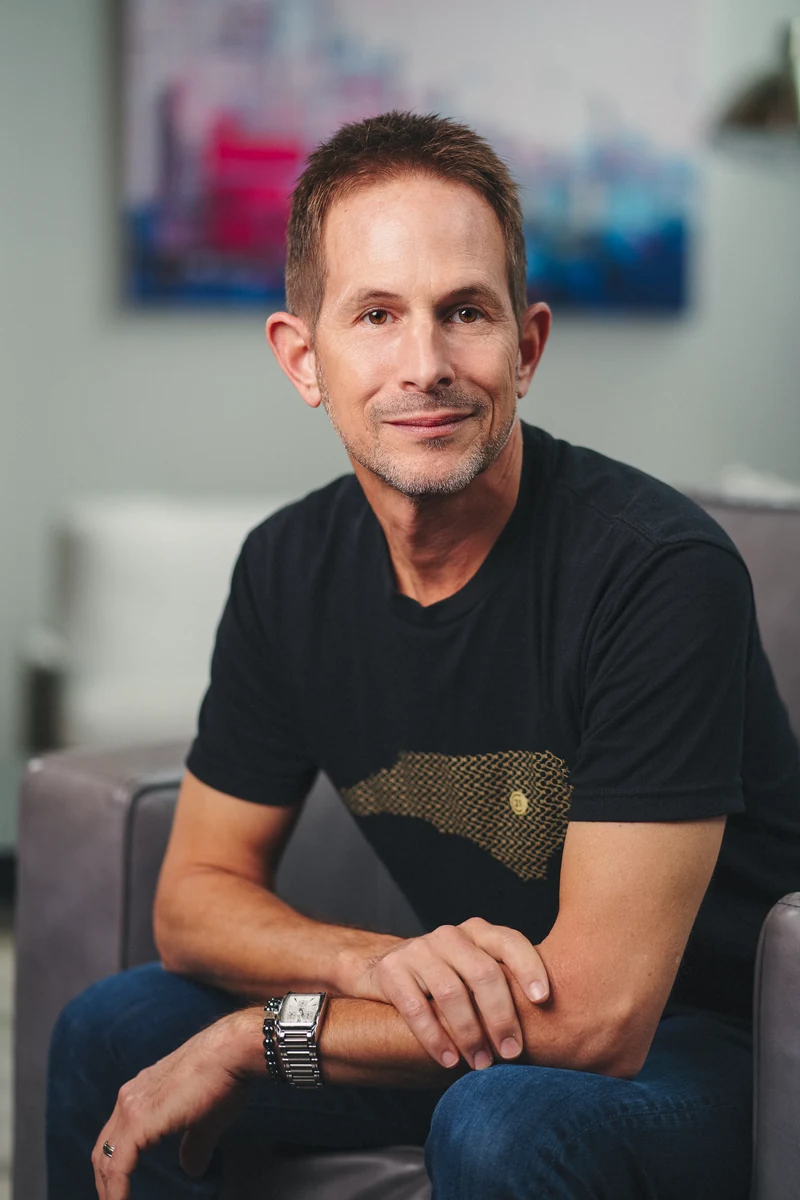Man in a black shirt seated in a softly lit gray office