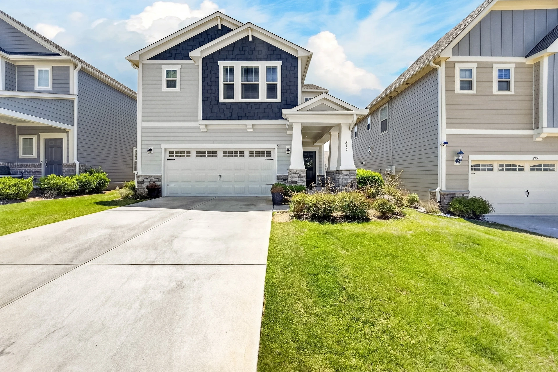 Front exterior of a gray and navy home with an attached garage, driveway, and landscaped lawn