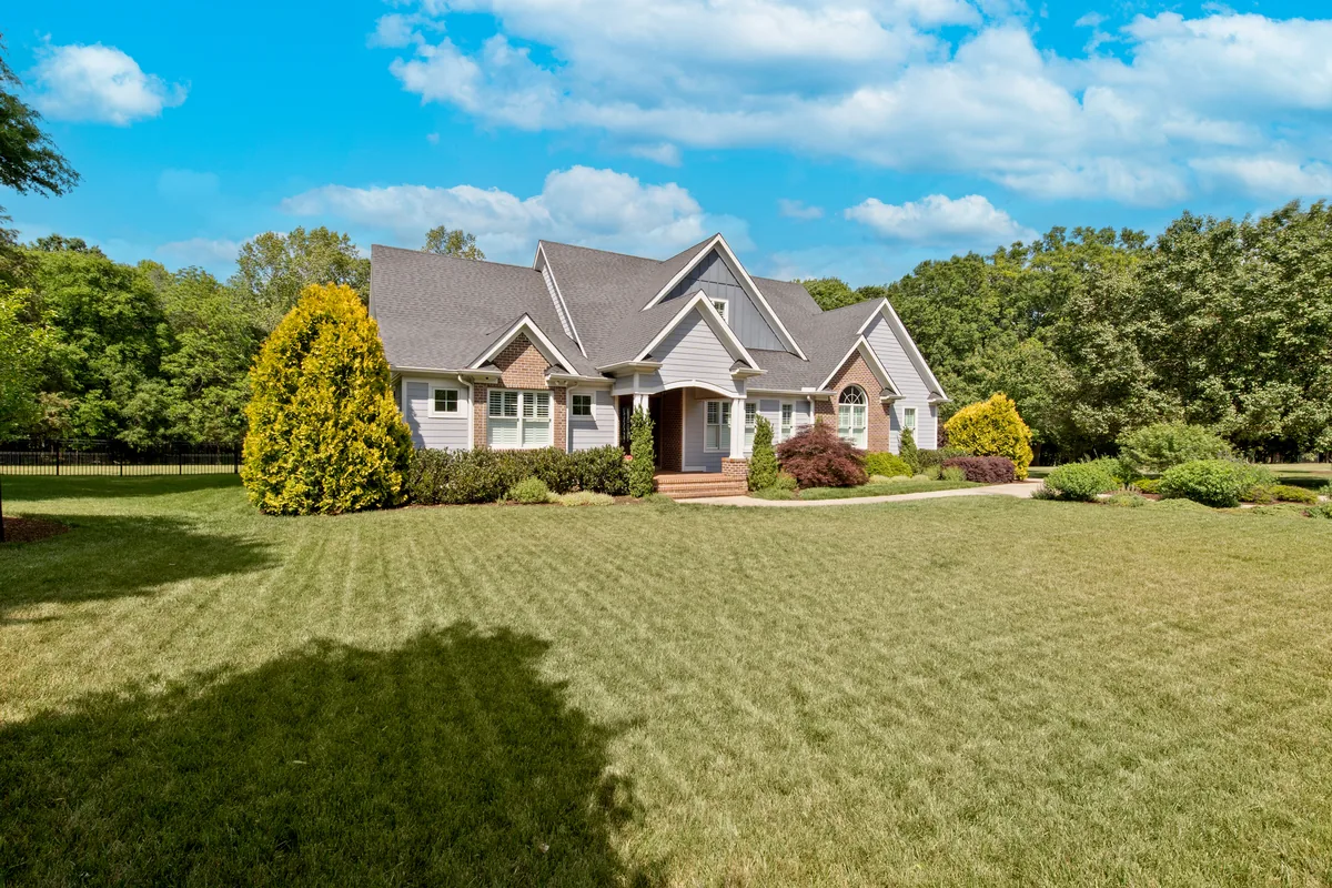 Traditional gray and brick home with a broad front lawn under a blue sky