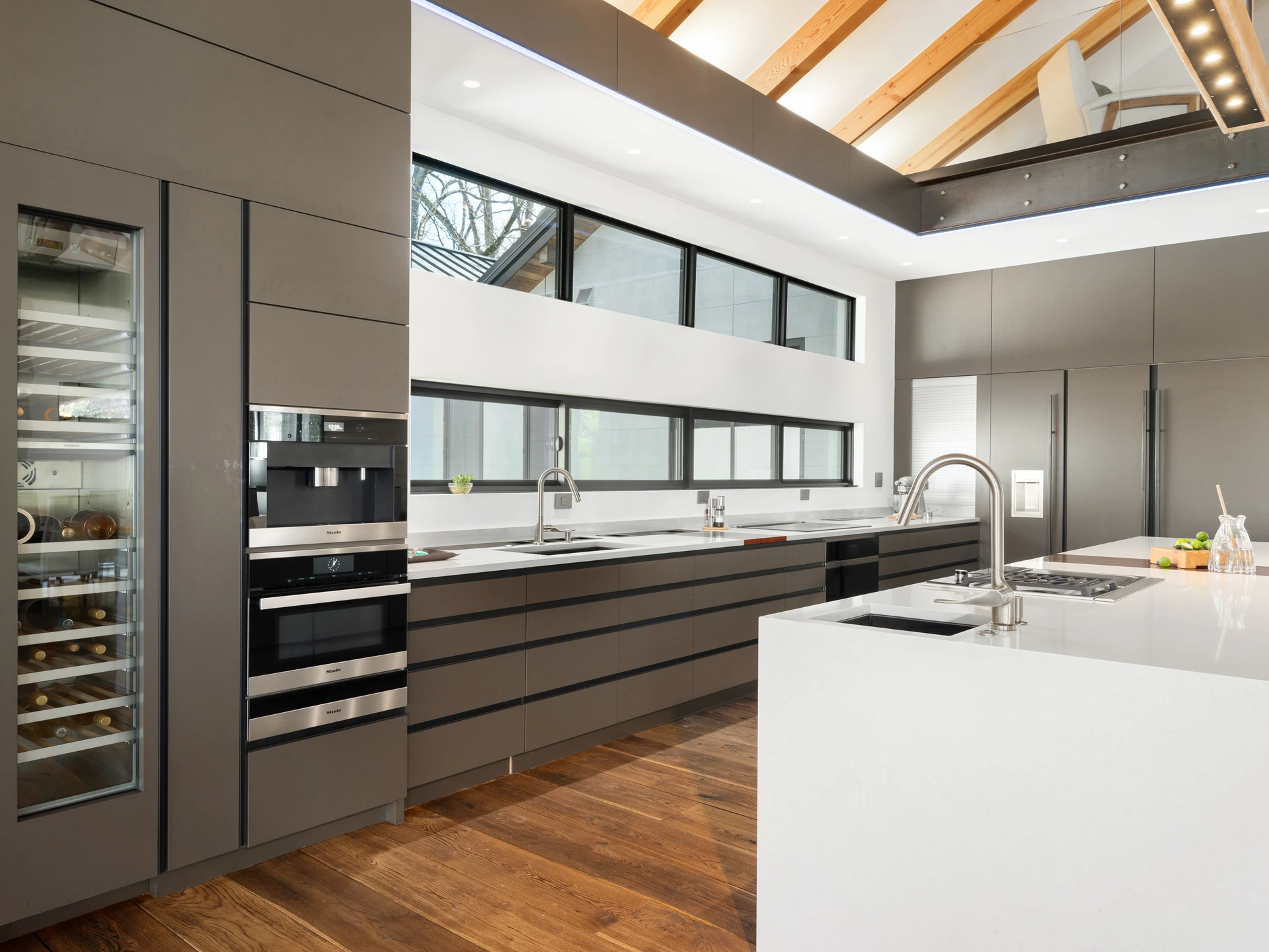 High-end kitchen with a large island, dark cabinetry, exposed ceiling beams, and a wall of windows