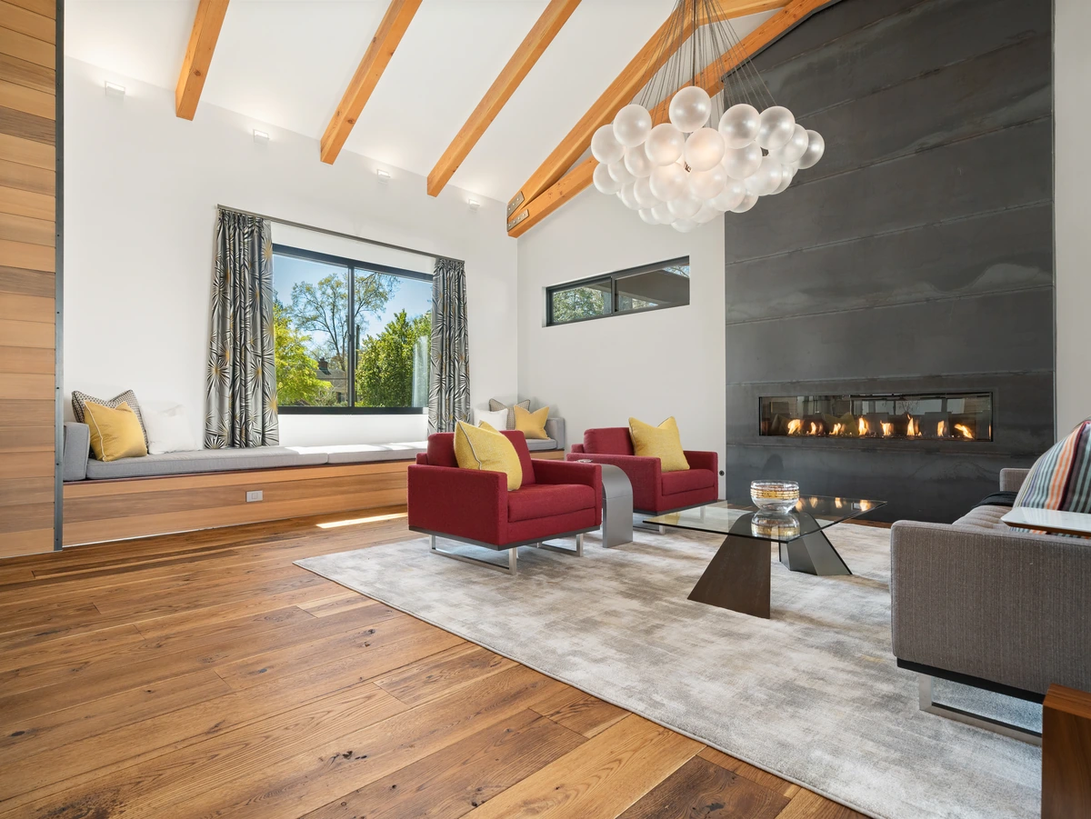 Luxury living room with red lounge chairs, a linear fireplace, broad windows, exposed ceiling beams, and built-in window seating