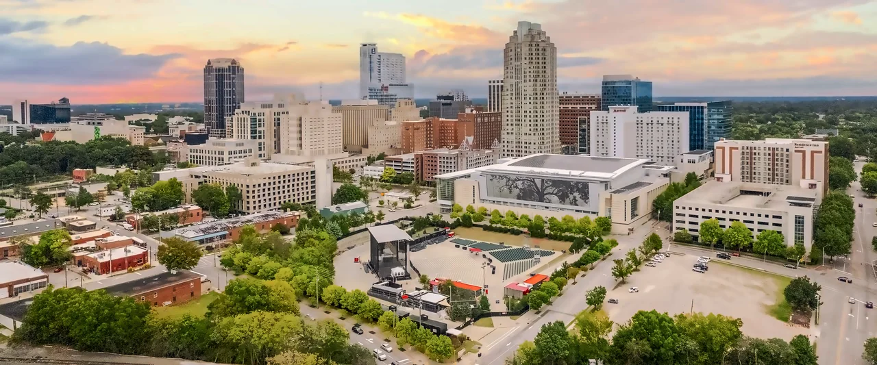 Downtown buildings and trees beneath a warm sunset sky in the RDU area