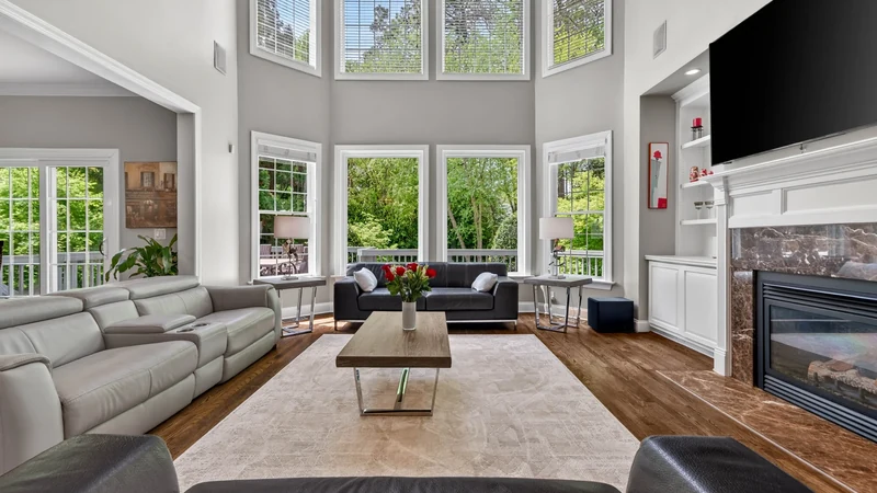 Bright professionally photographed living room with large windows and a fireplace.